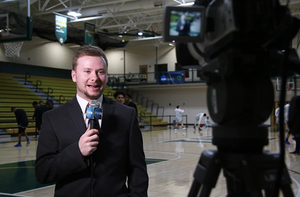 A young man holding a microphone at a live basketball game.